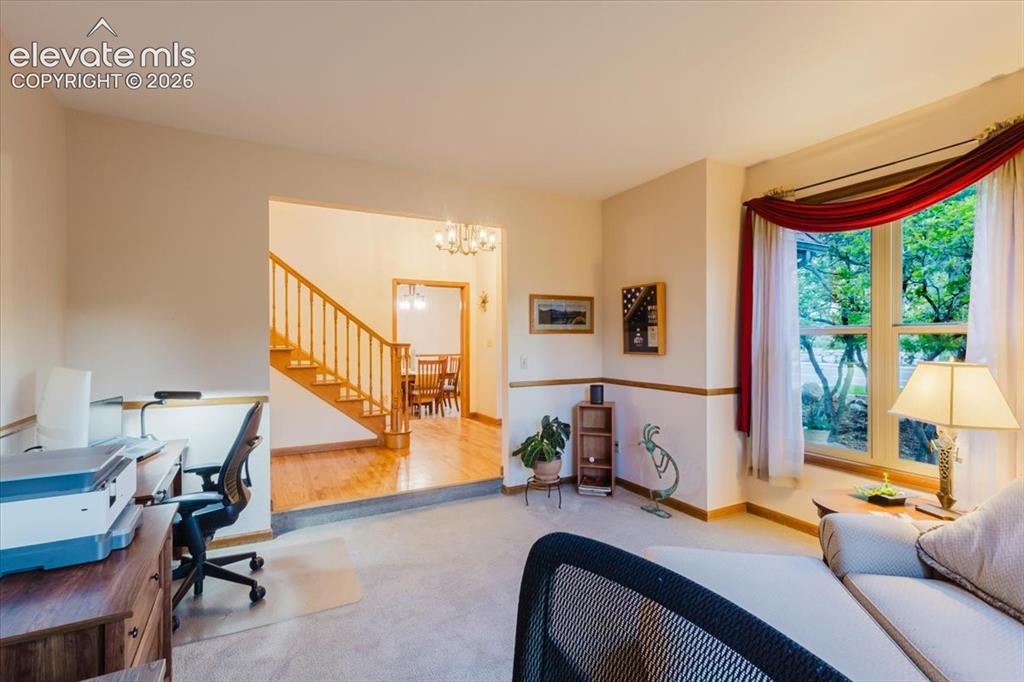 Image 8 of 50: Carpeted living area with a large bay window, stairway access to upper leve