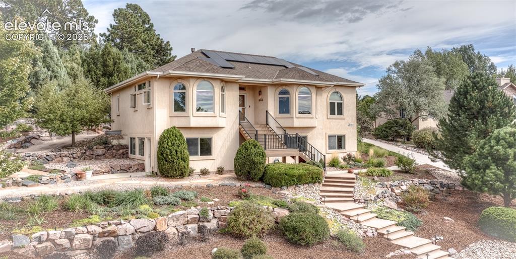 Caption: Stucco exterior with multiple arched windows, prominent solar panels, and a terraced front yard