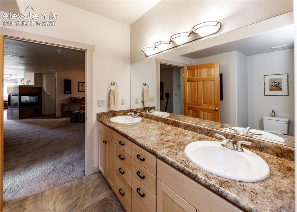 Image 32 of 50: Double vanity with integrated sinks, wood-finish cabinetry, and a large wal