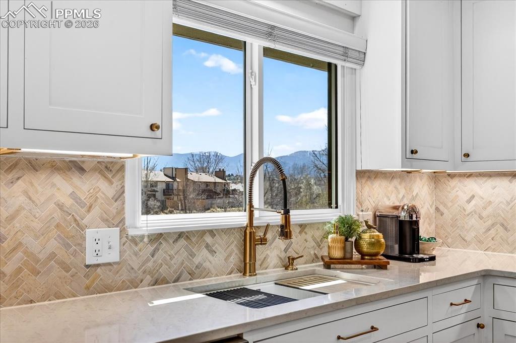 Image 10 of 48: Kitchen view of light stone counters, tasteful backsplash, and white cabine