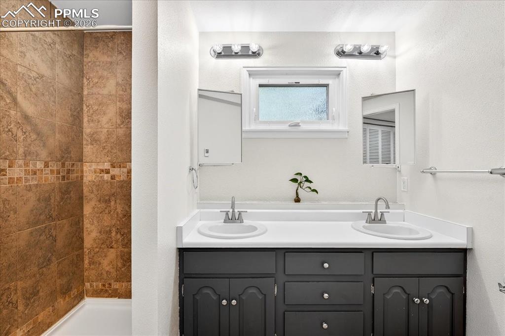 Image 28 of 48: Full bathroom with double vanity, a shower stall, and a textured wall
