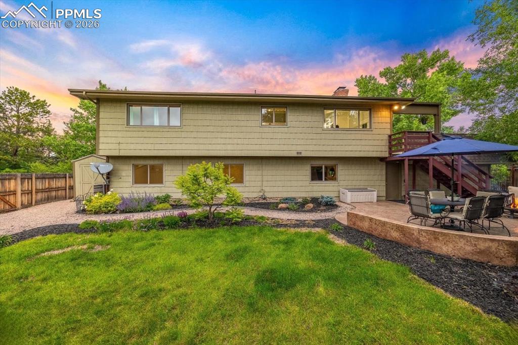 Image 44 of 48: Back of house at dusk with a patio area, a fenced backyard, a chimney, a sh
