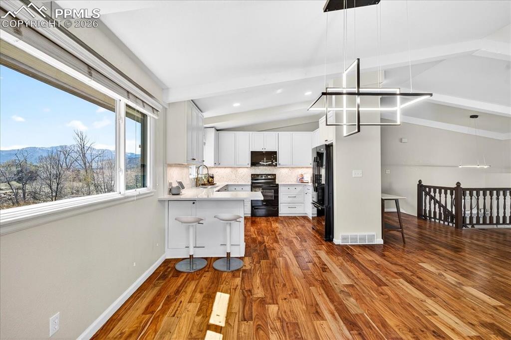 Image 6 of 48: Kitchen with black appliances, dark wood finished floors, a kitchen bar, ba