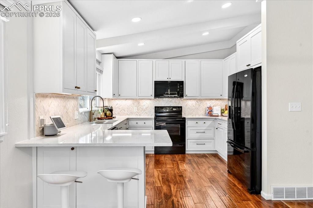 Image 7 of 48: Kitchen featuring a peninsula, white cabinets, black appliances, decorative