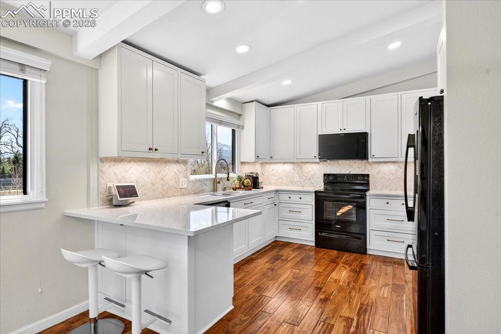 Image 8 of 48: Kitchen featuring black appliances, white cabinetry, a peninsula, tasteful 