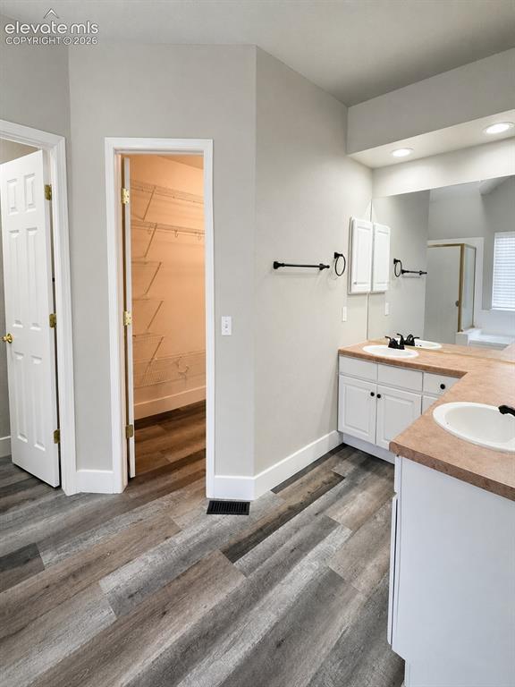 Image 11 of 25: Dual vanity with white cabinetry and integrated sinks, wood-finish flooring