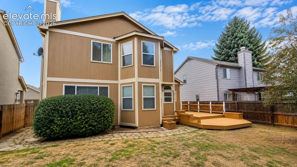 Image 24 of 25: Multi-level wood deck with railing, stone paver pathway, and mature landsca