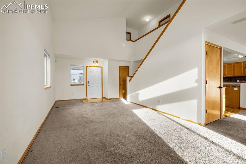Image 13 of 40: Unfurnished living room with light colored carpet, high vaulted ceiling, an