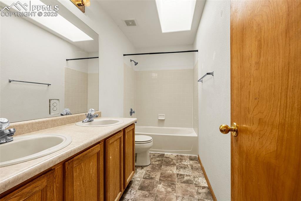 Image 22 of 40: Full bathroom featuring double vanity, shower / tub combination, a skylight