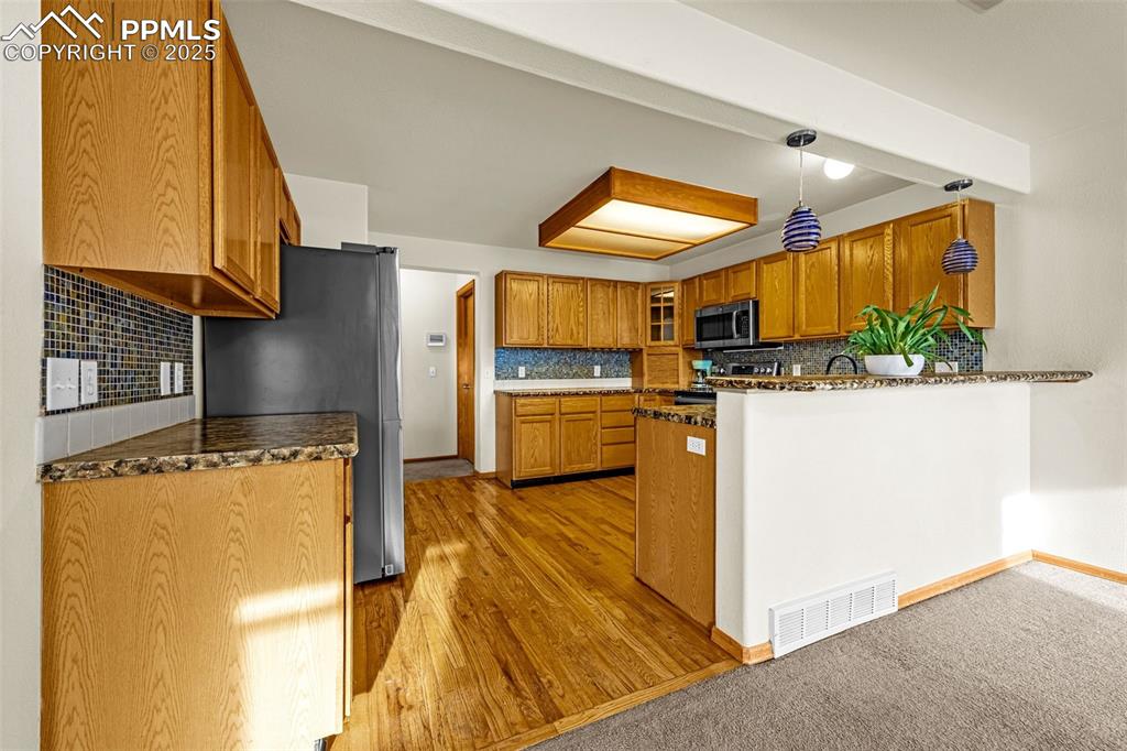 Image 4 of 40: Kitchen with stainless steel microwave, stove, brown cabinets, a peninsula,