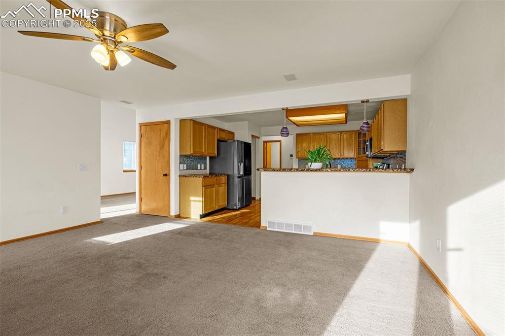 Image 9 of 40: Unfurnished living room featuring dark colored carpet and a ceiling fan