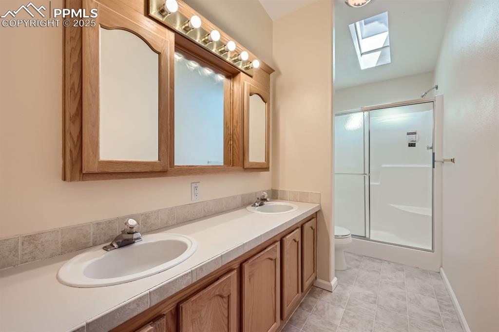 Image 16 of 28: Full bath featuring a skylight, a shower stall, and double vanity