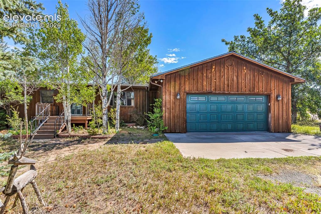 Image 1 of 49: Wood-paneled exterior featuring a prominent teal garage door with decorativ