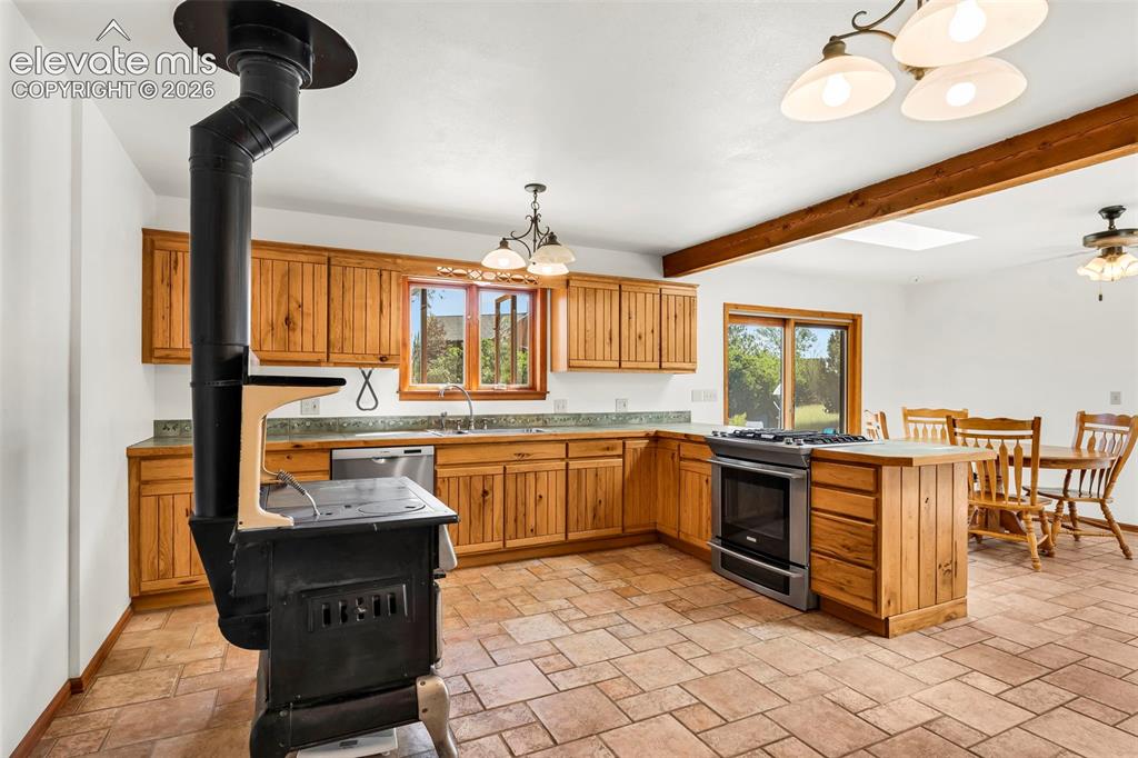 Image 12 of 49: Open concept kitchen featuring a wood-burning stove, natural wood cabinetry