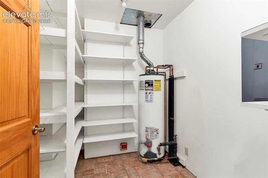 Image 17 of 49: Utility room featuring a water heater, terracotta-style flooring, white wal