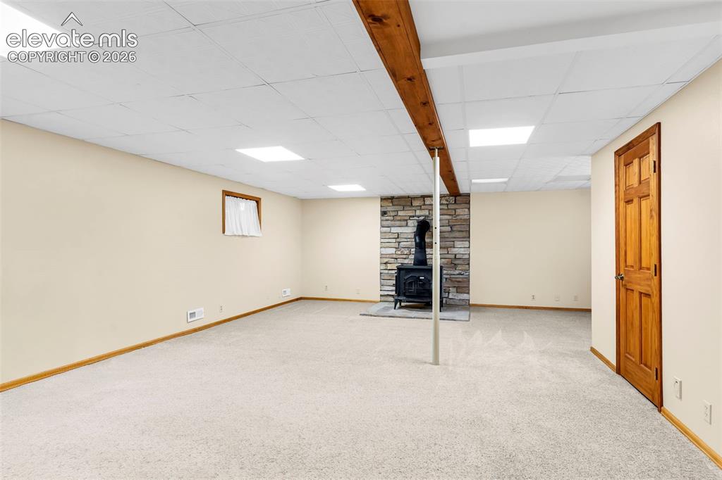 Image 22 of 49: Spacious finished basement featuring a stone-clad wood-burning stove, light