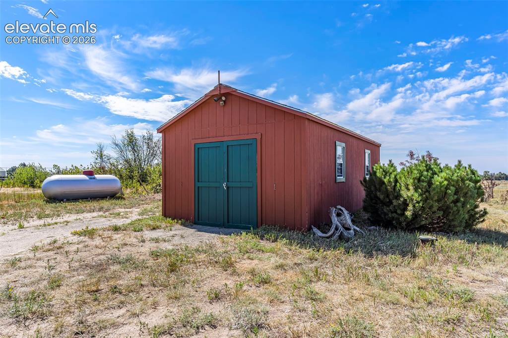 Image 35 of 49: Red storage shed with green double doors, two windows, and a gabled roof