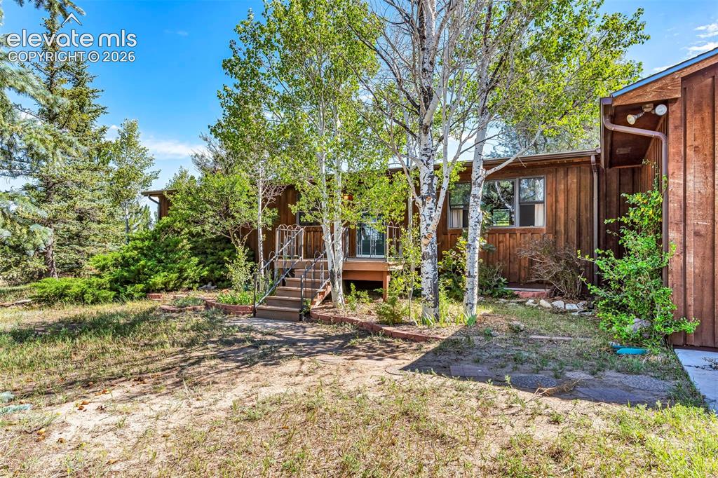 Image 5 of 49: Wood-sided exterior featuring mature trees and established landscaping