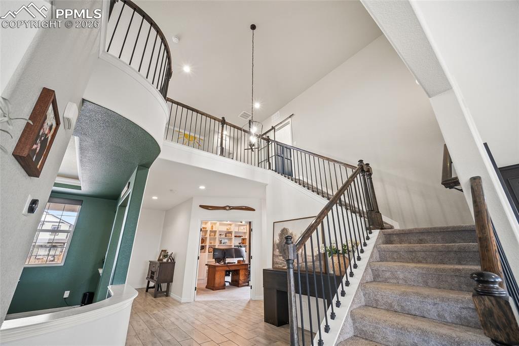 Image 7 of 50: Stairs featuring recessed lighting, wood finished floors, and a towering ce