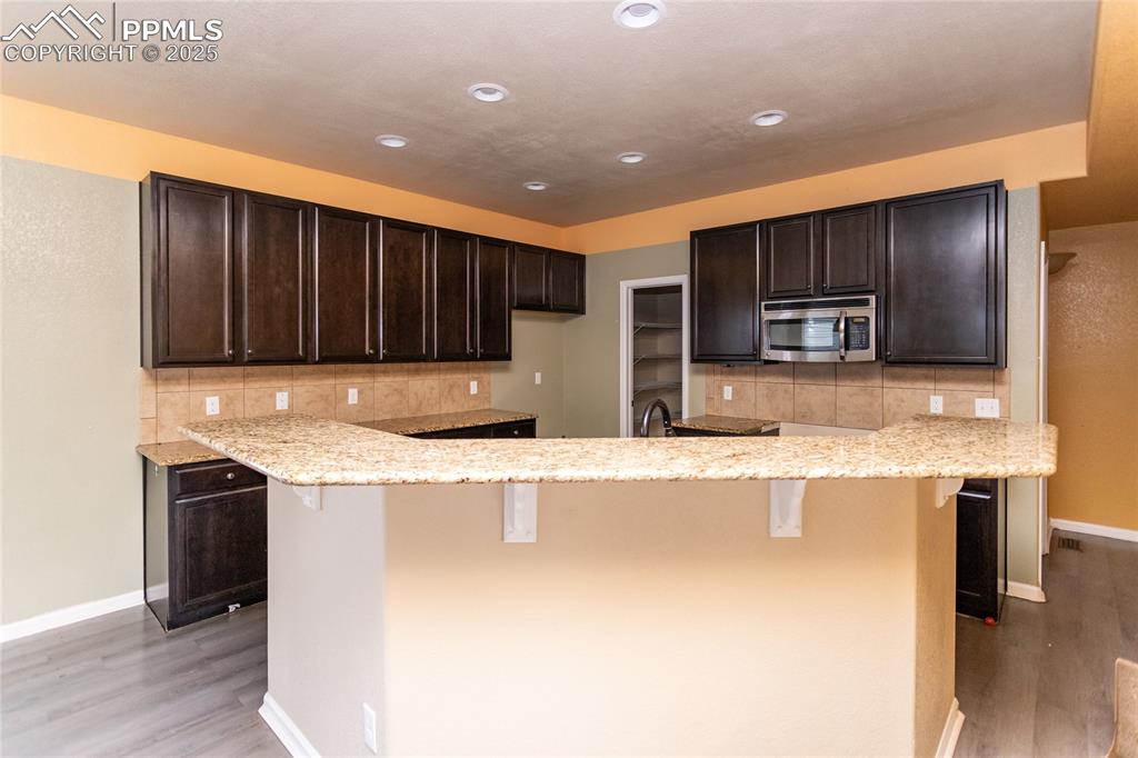Image 11 of 49: Kitchen featuring a breakfast bar area, dark brown cabinets, light wood fin
