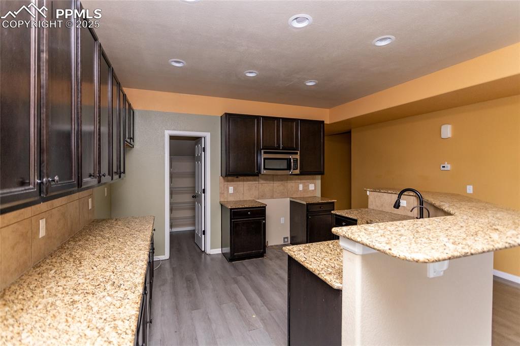 Image 12 of 49: Kitchen with dark brown cabinets, decorative backsplash, light stone counte