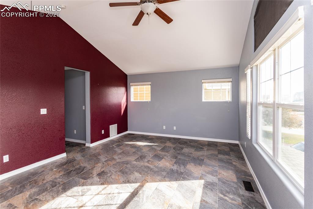 Image 22 of 49: Primary bedroom with stone finish floors, ceiling fan, and lofted ceiling