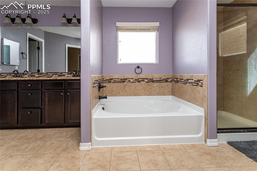Image 27 of 49: Full bath with a bath, light tile patterned floors, double vanity, and a st