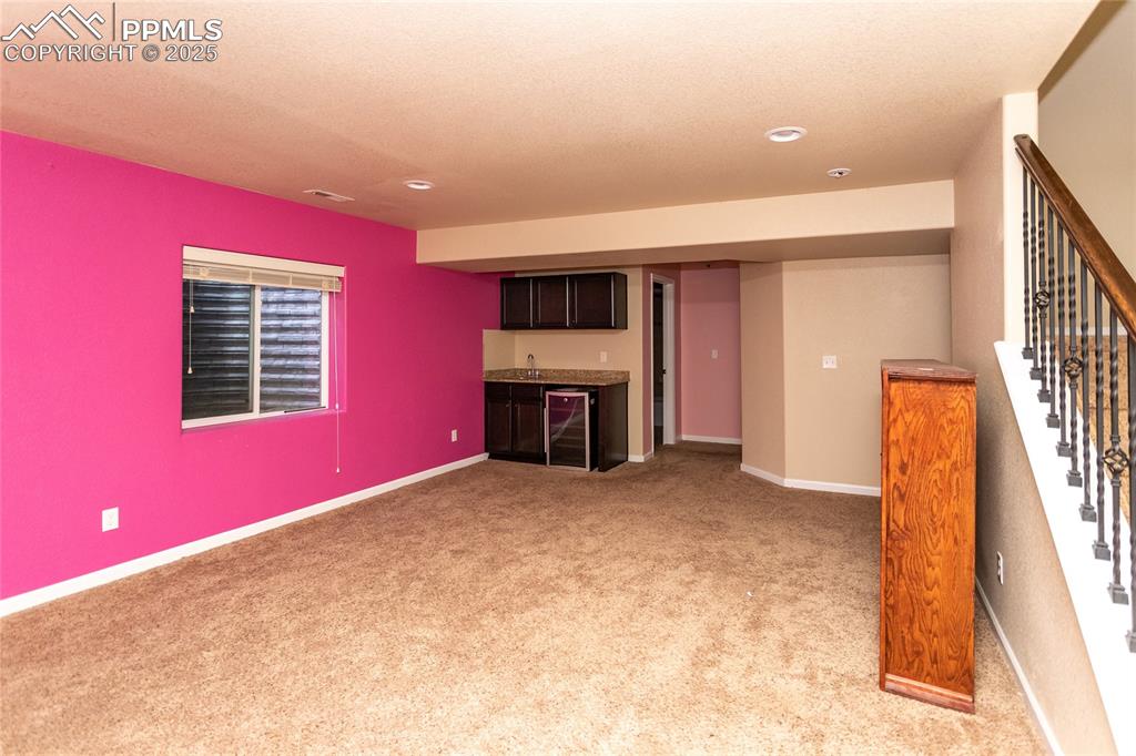 Image 39 of 49: Unfurnished basement with light carpet, bar with sink, wine cooler, stairwa
