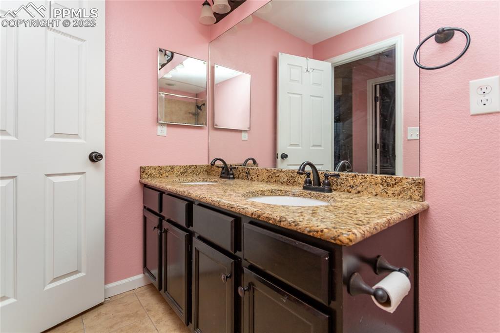 Image 40 of 49: Full bath with double vanity, light tile patterned floors, and a textured w