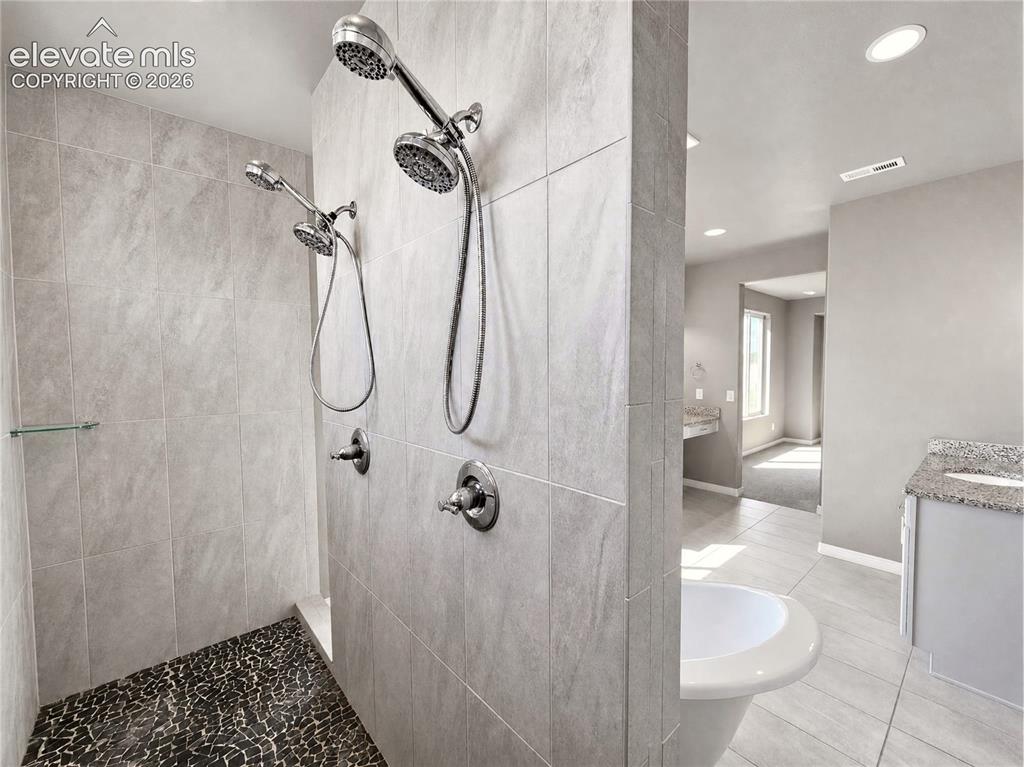 Image 17 of 35: Walk-in shower with dual shower heads, light-toned tile walls, and a pebble