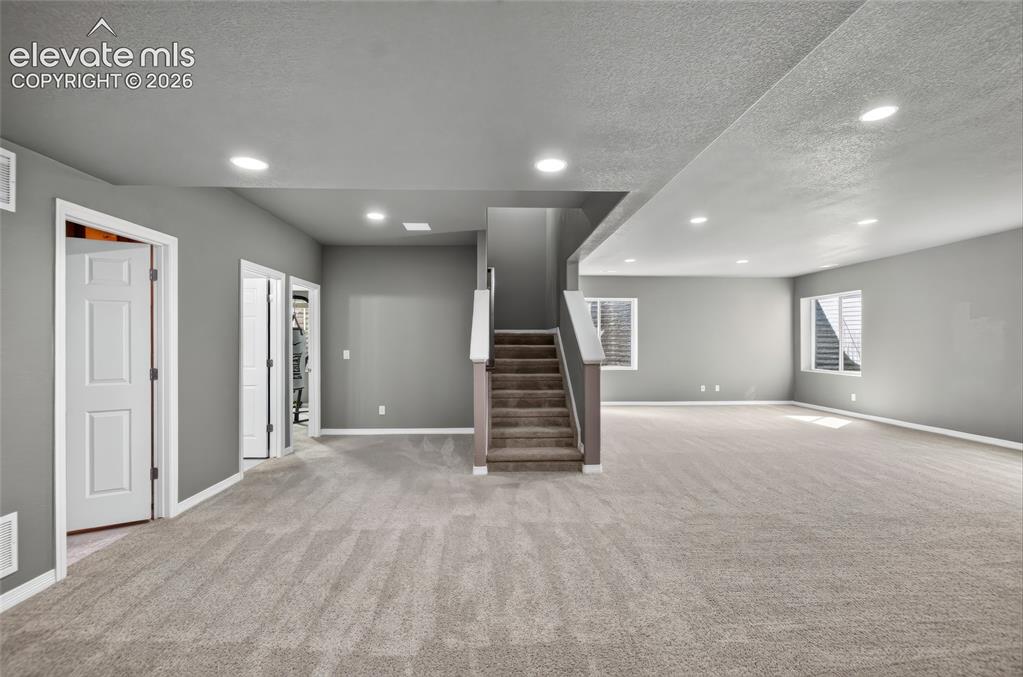 Image 24 of 35: Expansive carpeted area, recessed lighting, two windows with blinds, and a