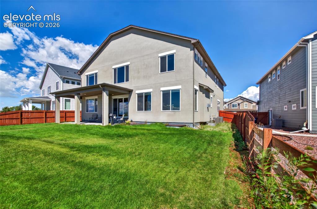 Image 29 of 35: Expansive green lawn, covered patio, stucco exterior, privacy fencing, and