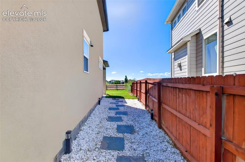 Image 30 of 35: Stucco and siding exterior with a wood fence, white gravel pathway, and rec