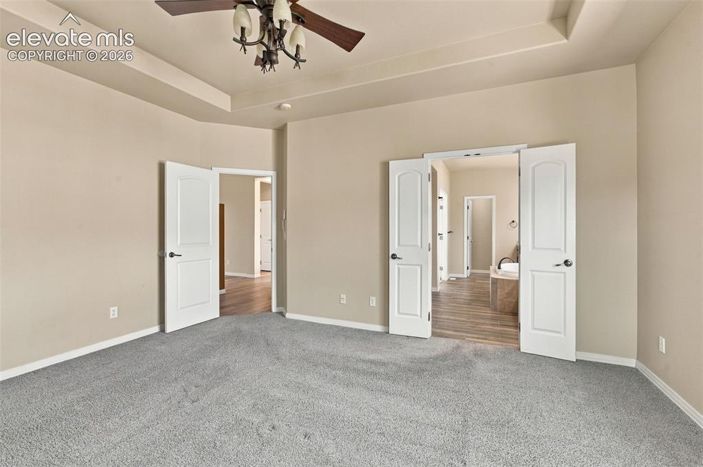 Image 21 of 48: Tray ceiling featuring a multi-light ceiling fan, neutral carpeting, and wh
