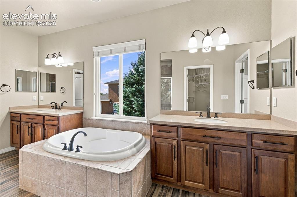 Image 23 of 48: Dual wood-finish vanities with solid-surface countertops, soaking tub with