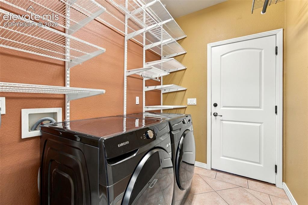 Image 29 of 48: Laundry room featuring multi-tier white wire shelving, tile flooring, and a