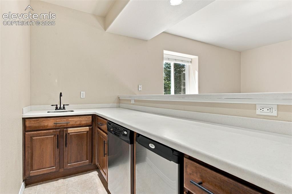Image 33 of 48: Wet bar featuring wood cabinetry, solid-surface countertops, an undermount 