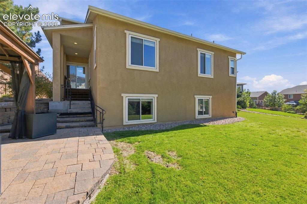 Image 42 of 48: Stucco exterior featuring dual-level window placements, stone paver patio,