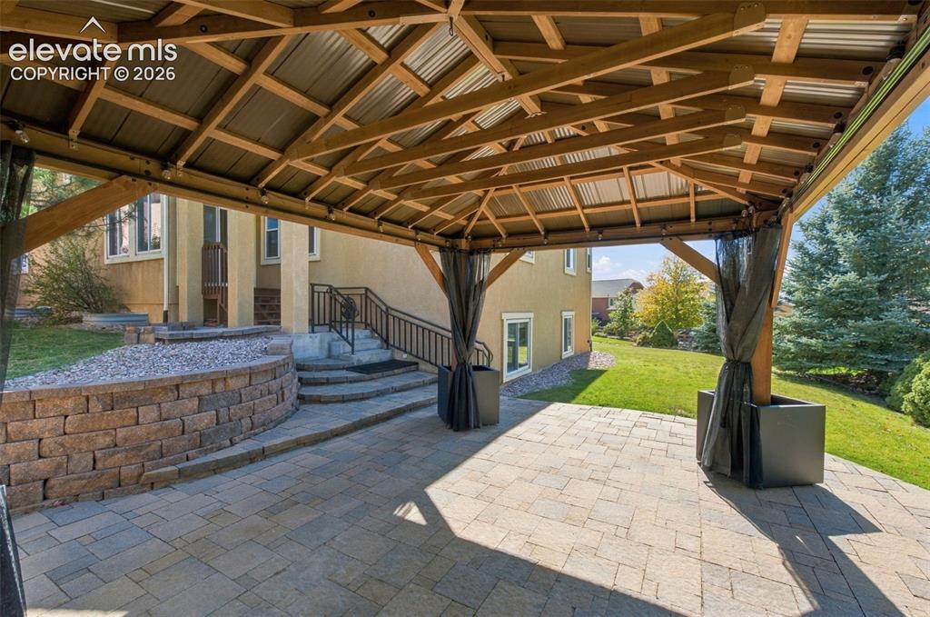 Image 44 of 48: Covered patio with a timber-frame structure and metal roof, stone paver flo