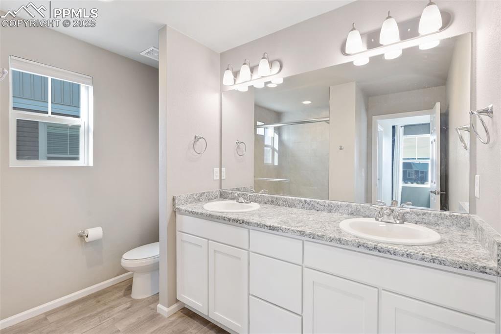 Image 19 of 39: Bathroom with double vanity, a stall shower, and light wood-style flooring