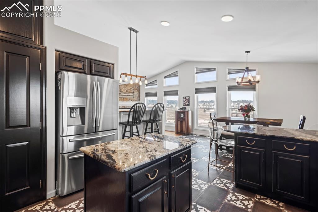Image 14 of 49: Kitchen featuring light stone counters, vaulted ceiling, a center island, s