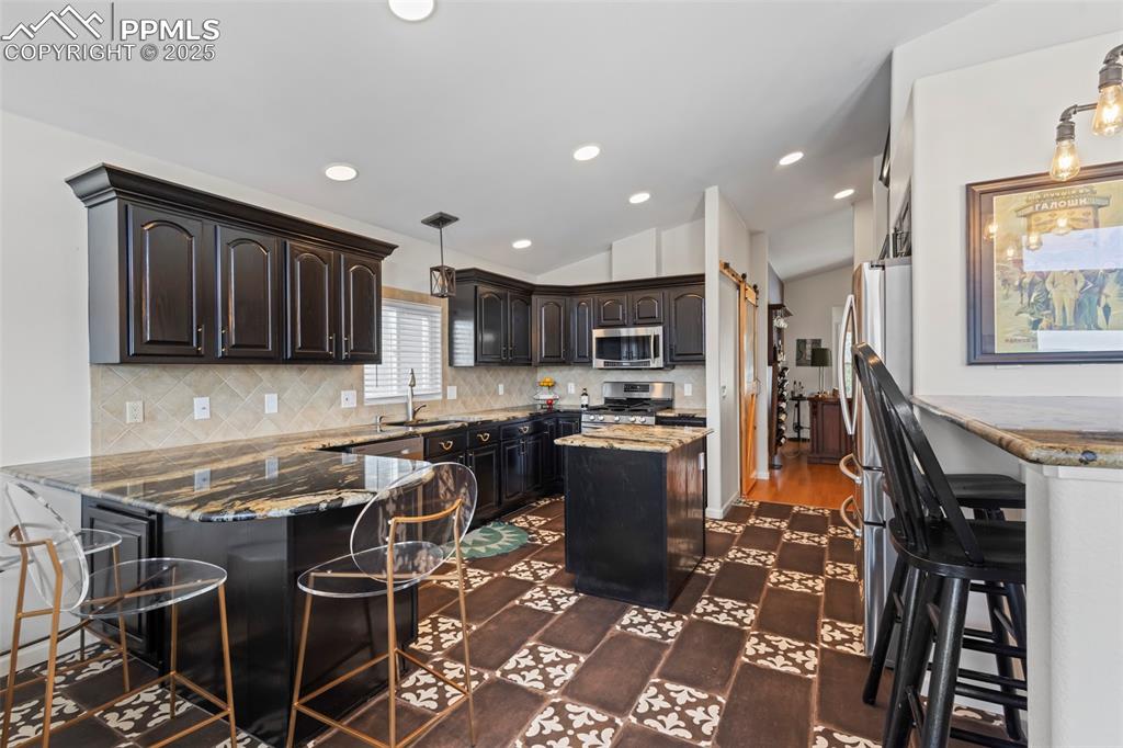 Image 15 of 49: Kitchen featuring appliances with stainless steel finishes, a breakfast bar