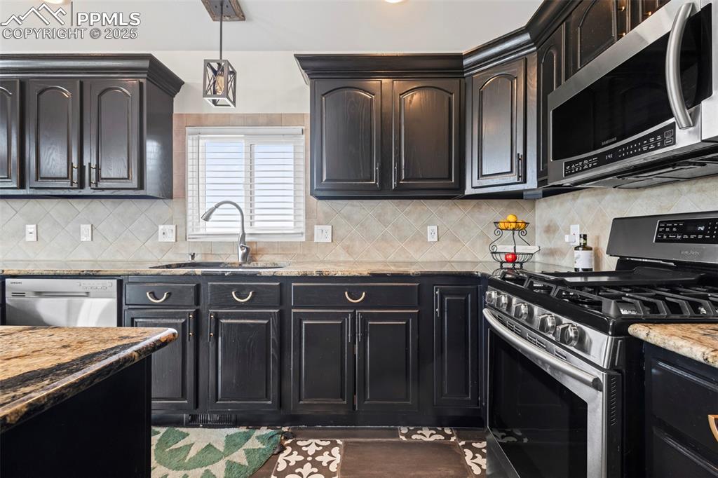 Image 16 of 49: Kitchen with light stone counters, stainless steel appliances, a sink, back