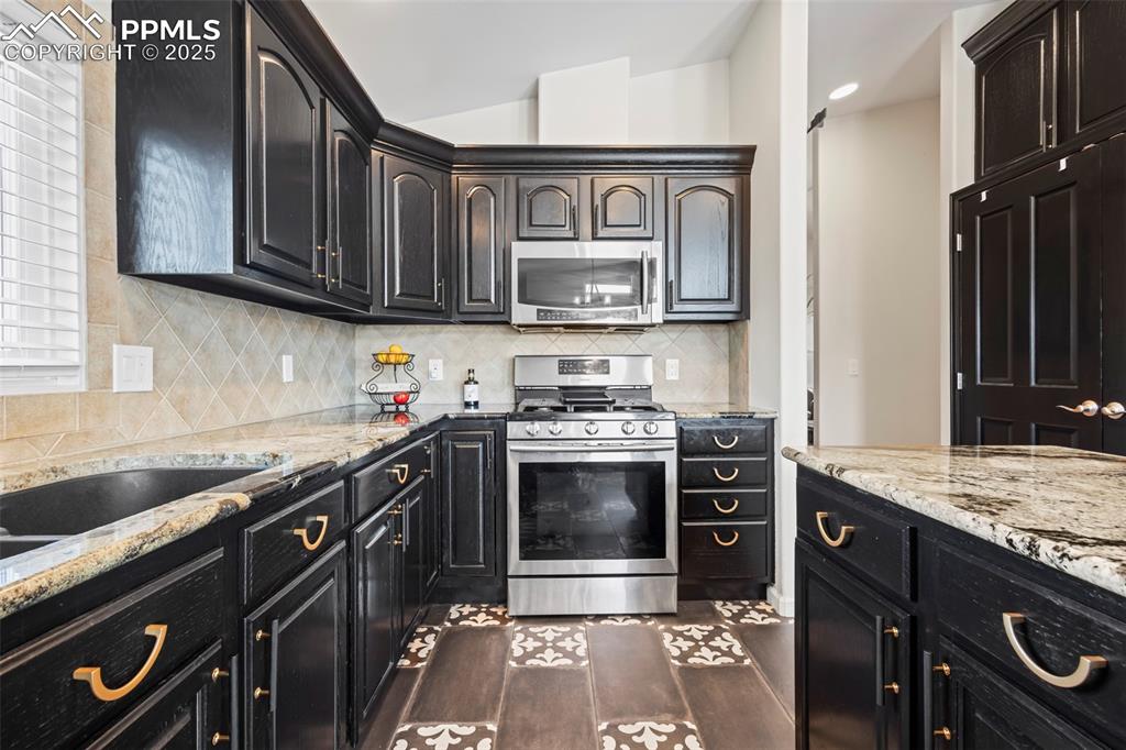 Image 17 of 49: Kitchen with dark wood-style flooring, stainless steel appliances, backspla