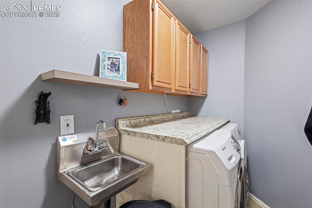 Image 26 of 49: Clothes washing area featuring cabinet space, washer and dryer, and a sink