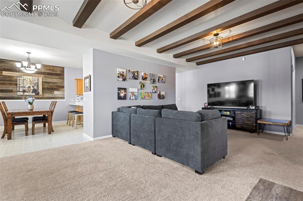 Image 33 of 49: Living room with baseboards, light colored carpet, beamed ceiling, wood wal
