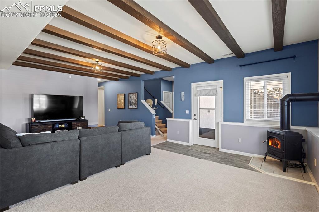 Image 34 of 49: Living room with baseboards, stairway, beamed ceiling, a wood stove, and ca