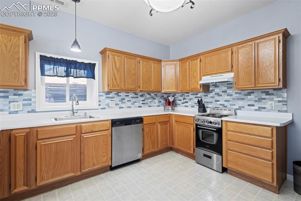 Image 38 of 49: Kitchen with under cabinet range hood, a sink, hanging light fixtures, appl