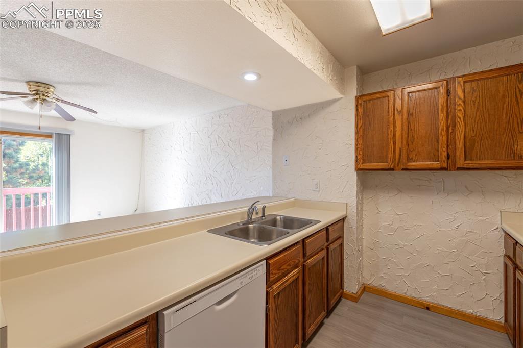 Image 10 of 31: Kitchen with a textured wall, brown cabinetry, light wood-style flooring, w