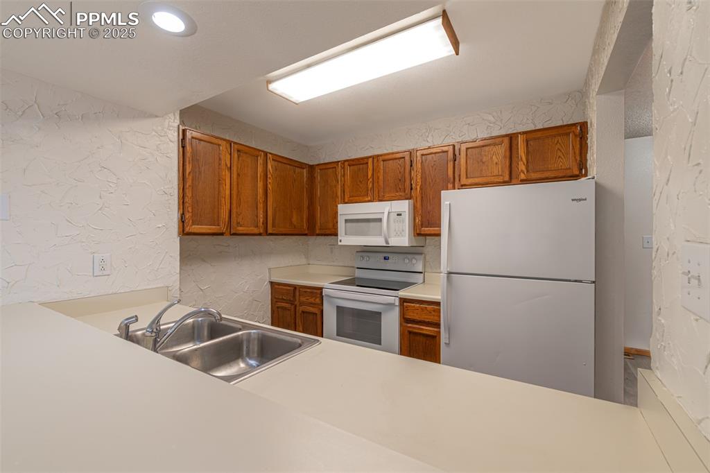 Image 11 of 31: Kitchen featuring a textured wall, brown cabinetry, white appliances, light